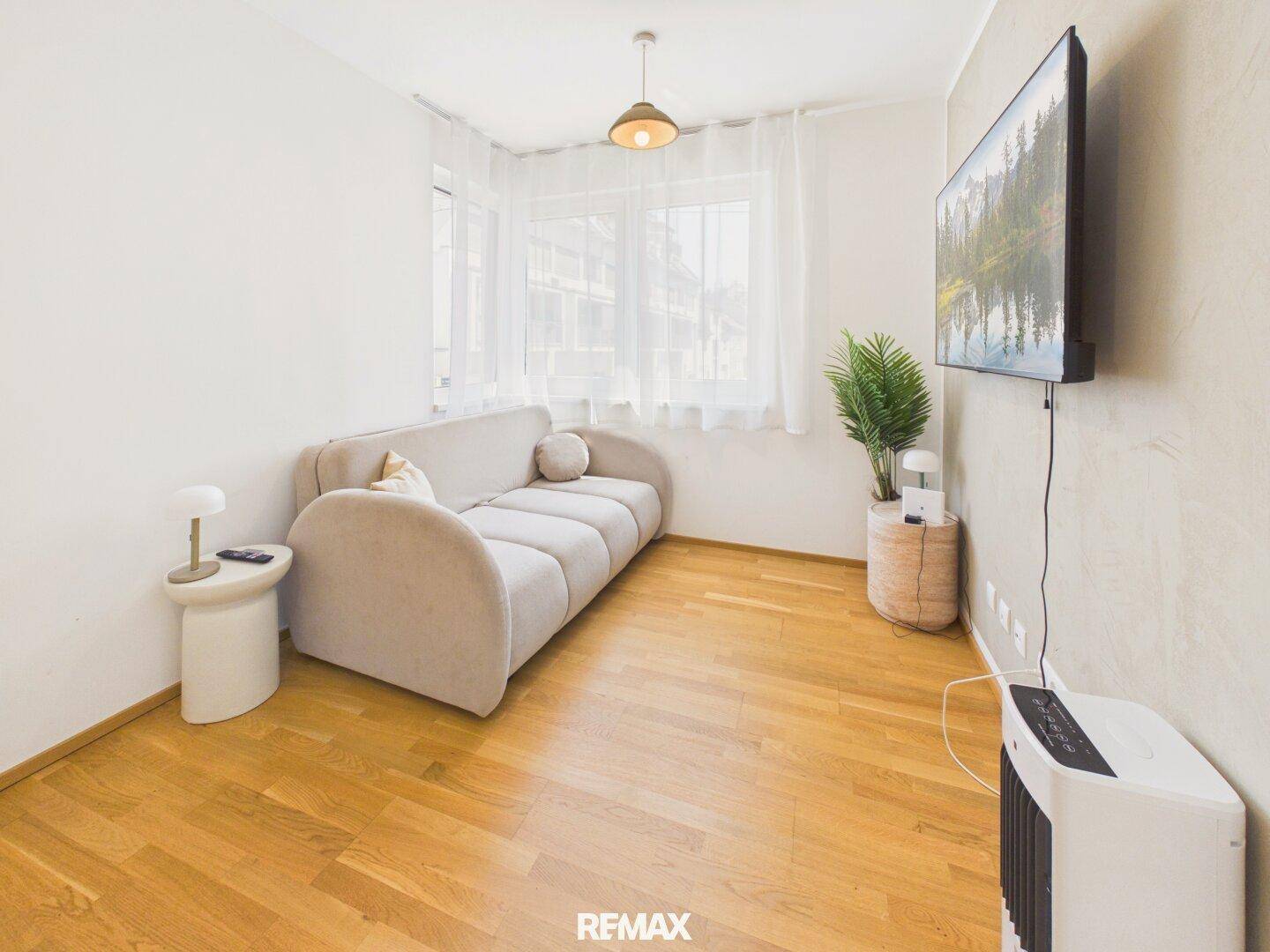 Gemütliches Wohnzimmer mit beigem Sofa, Holzboden und einem an der Wand montierten Fernseher.