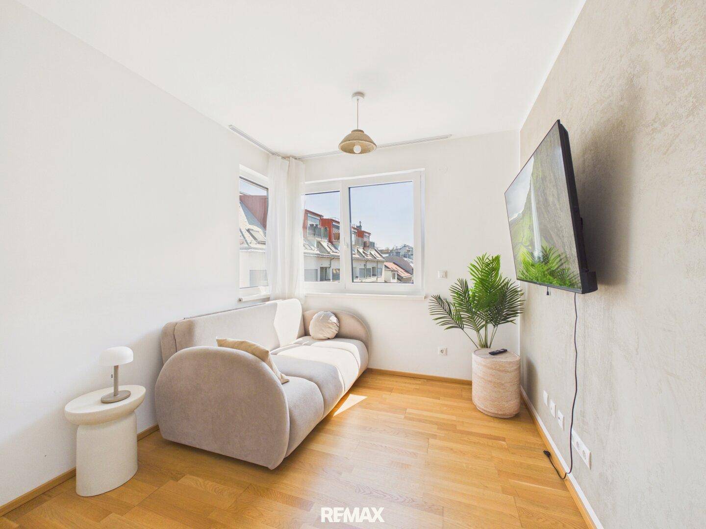 Helles Wohnzimmer mit beigem Sofa, Holzboden und Blick auf die umliegenden Gebäude.