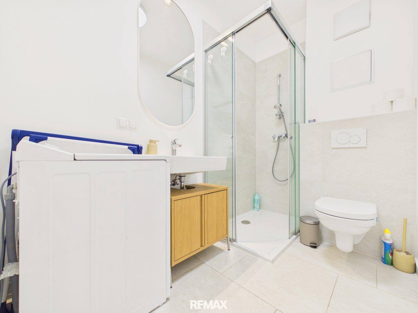 Modernes Badezimmer mit ebenerdiger Dusche, wandhängendem WC, Einzelwaschbecken und Waschmaschine.