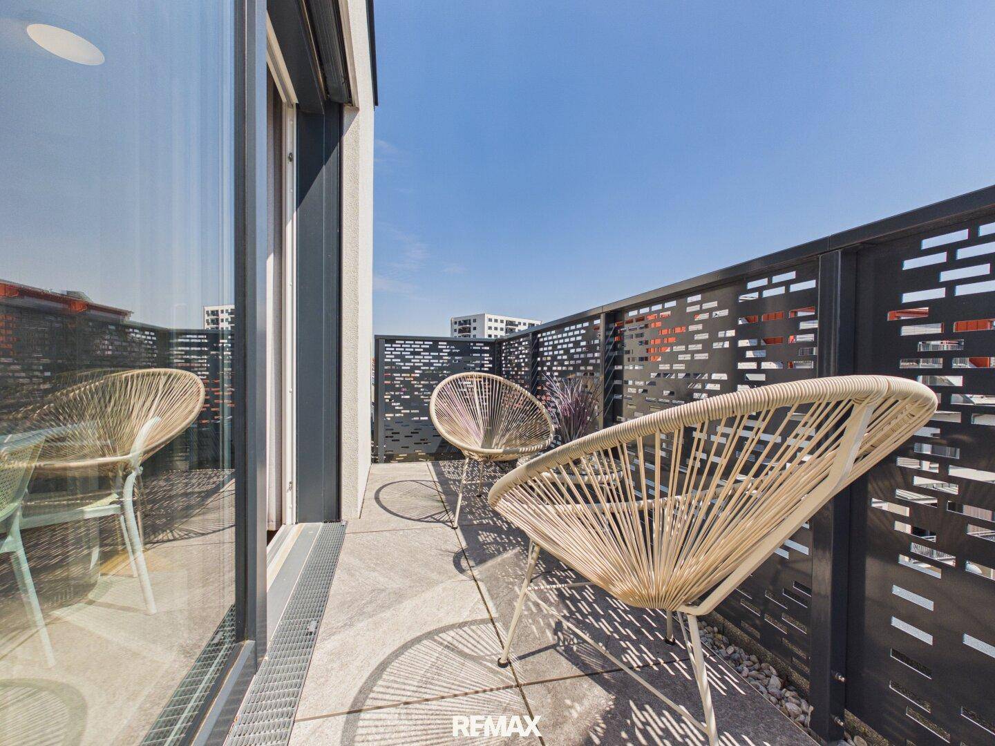 Sonniger Balkon mit modernen Möbeln und perforiertem Geländer, ideal zum Entspannen im Freien.