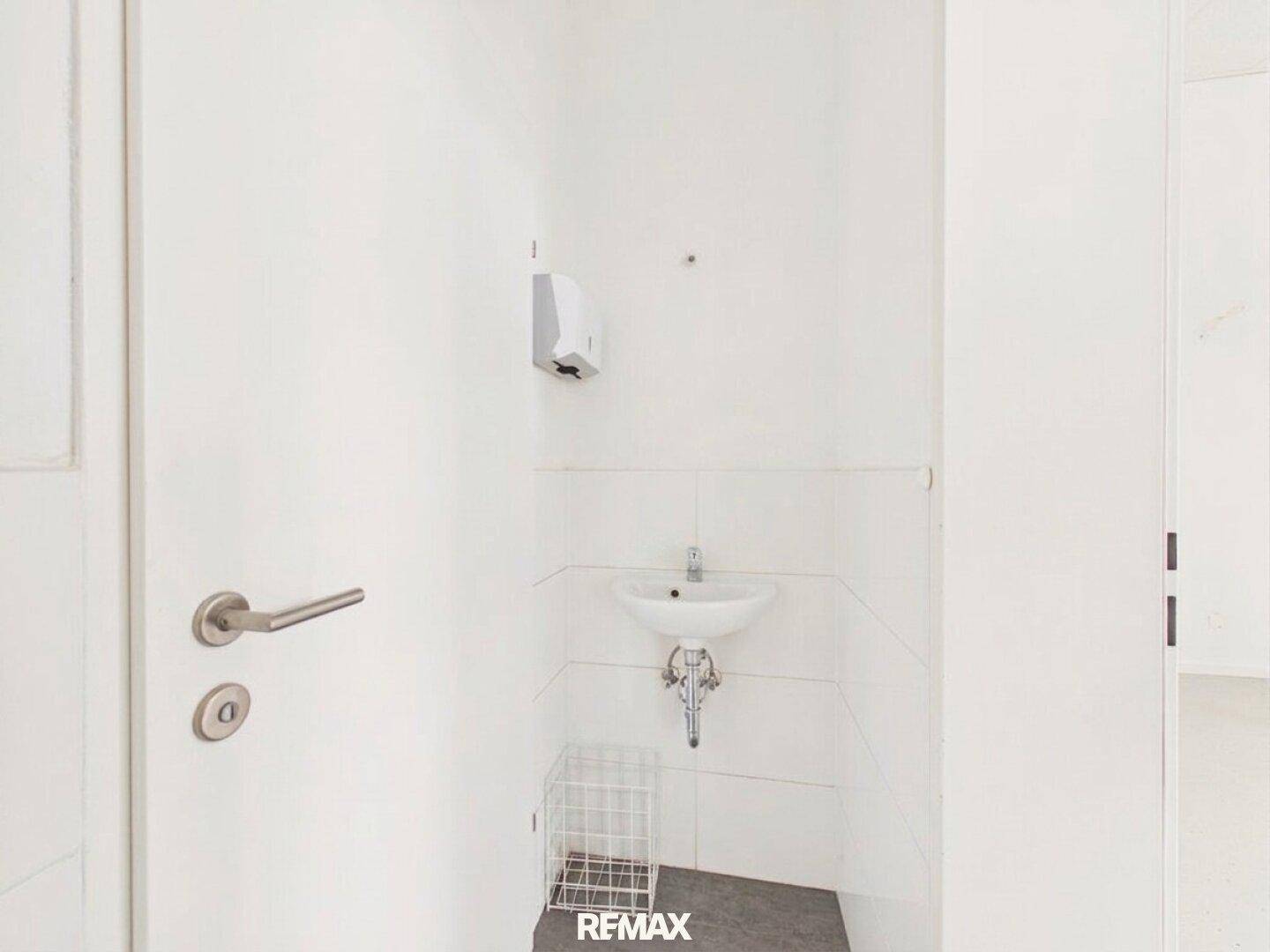 Kleiner Toilettenraum mit einem Waschbecken und weißen Fliesen, einfach und funktional gestaltet.