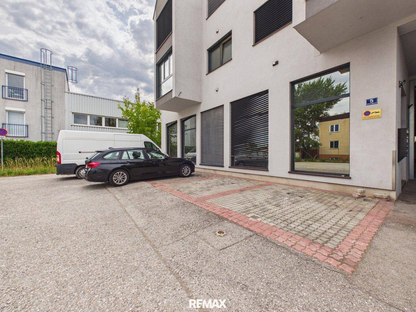Moderne Gebäudefassade mit großen Fenstern und davor liegenden Parkplätzen.