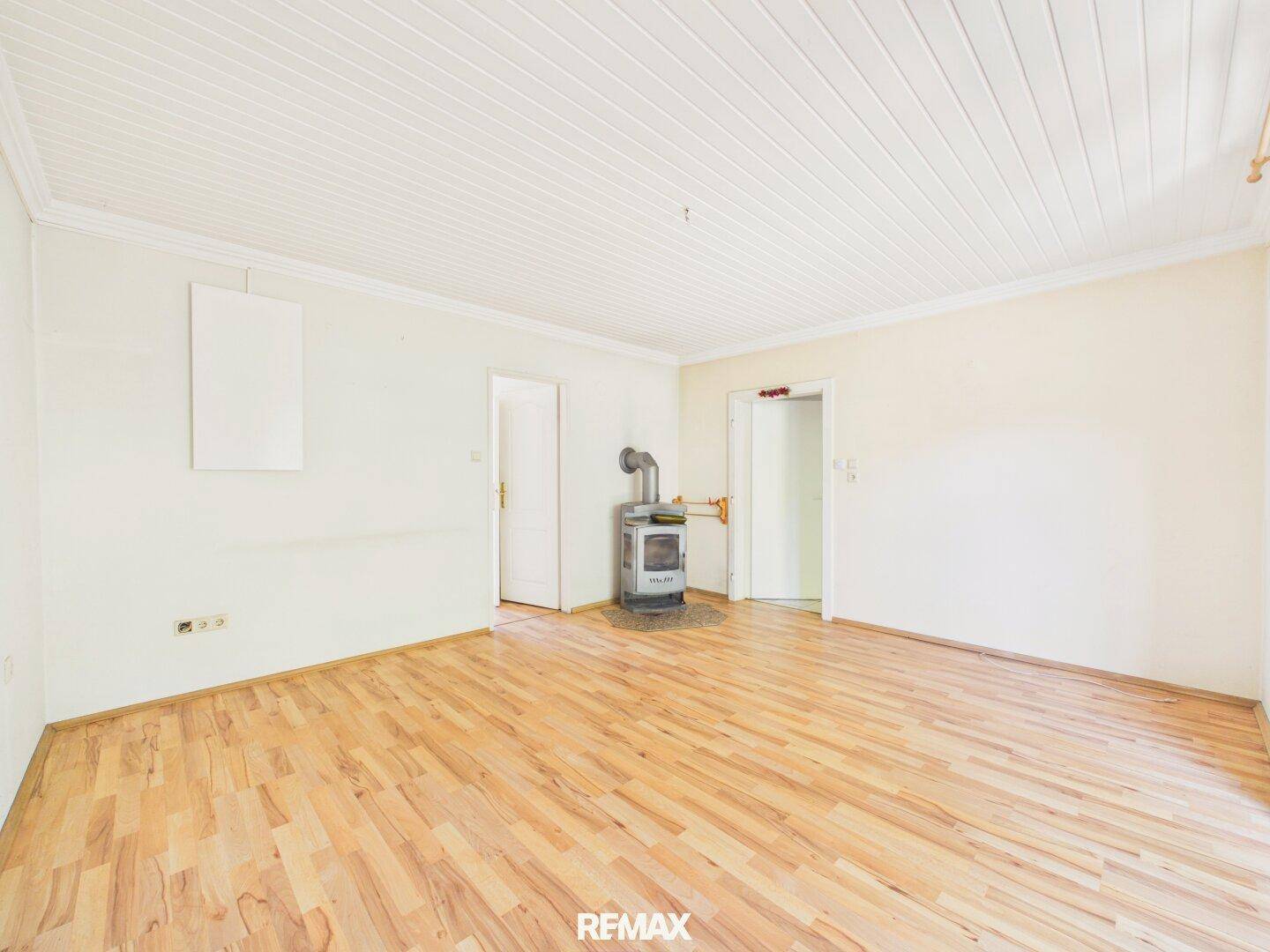 Leeres Wohnzimmer mit hellem Laminatboden und einem Holzofen als Heizquelle.