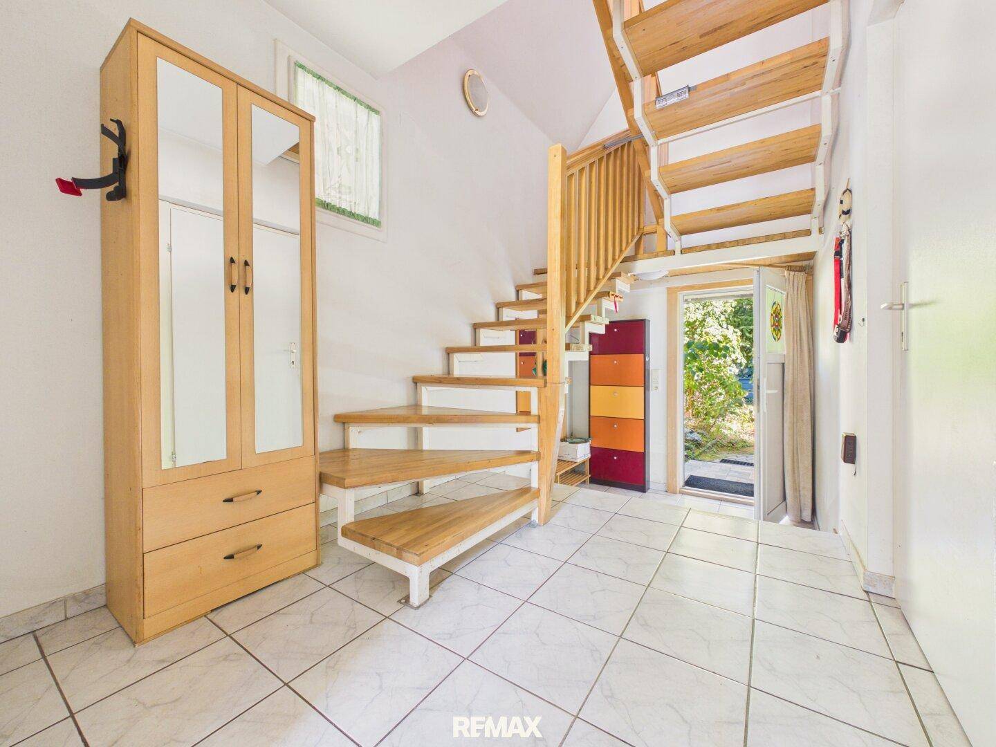 Heller Eingangsbereich mit gefliestem Boden, Holztreppe und Zugang zum Garten.