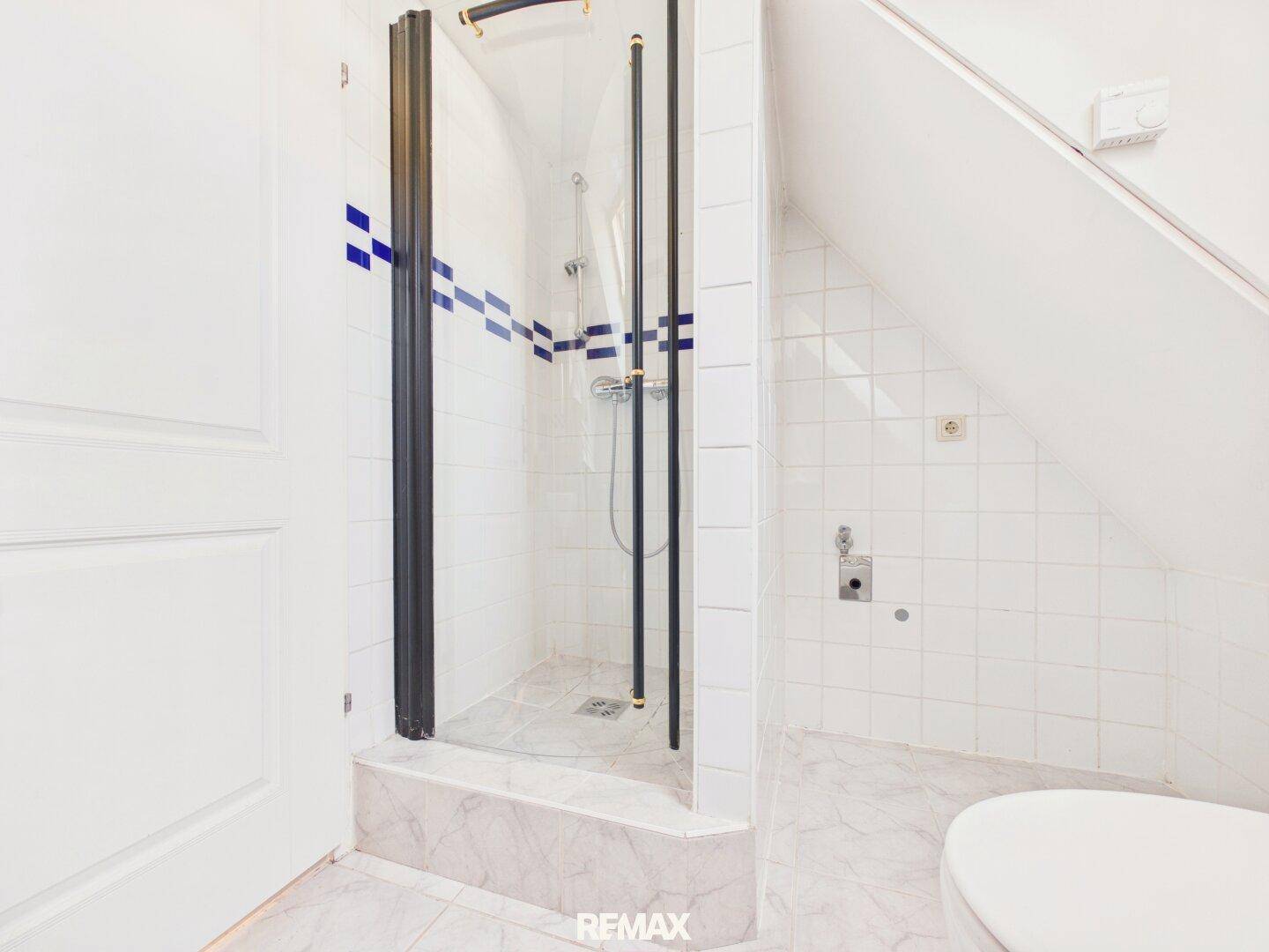 Badezimmer im Dachgeschoss mit Dusche, weißen Fliesen und Dachschrägen.