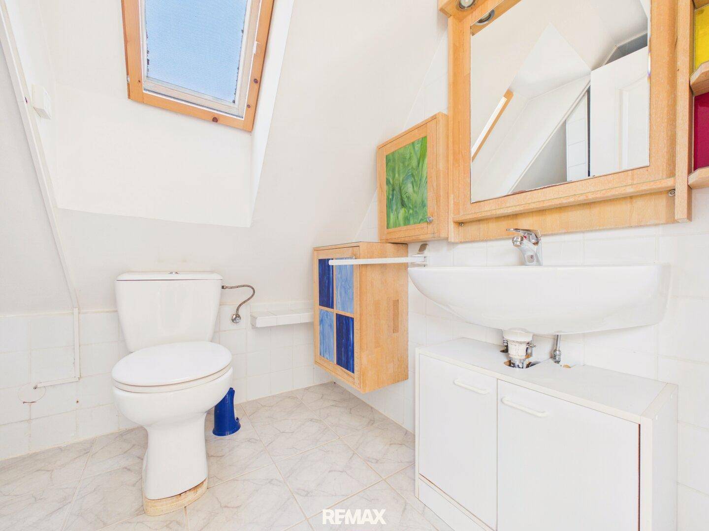 Helles Badezimmer im Dachgeschoss mit Waschbecken, Toilette und Dachfenster.