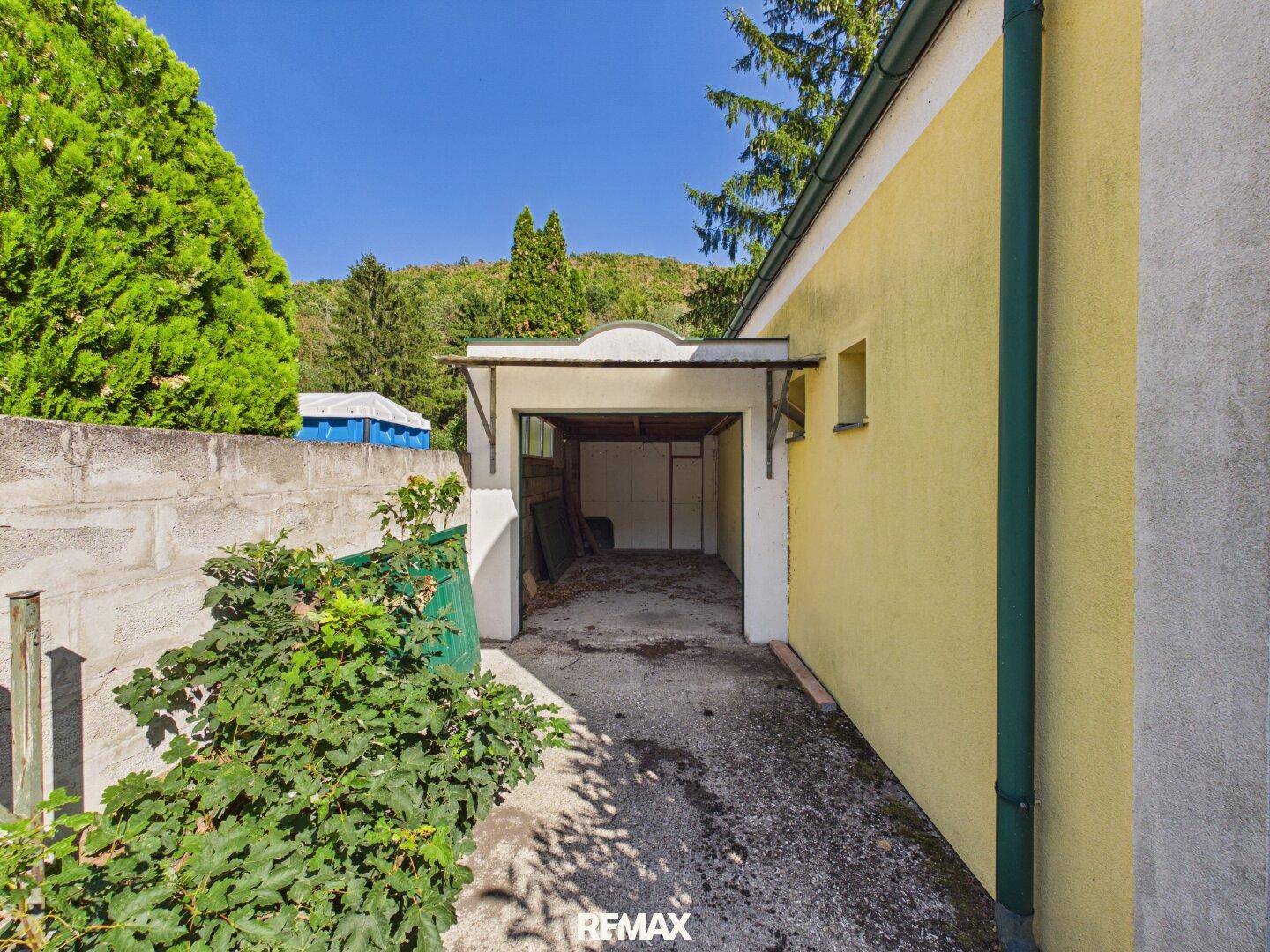 Einfahrt zu einer Einzelgarage, umgeben von Vegetation und einer Mauer.