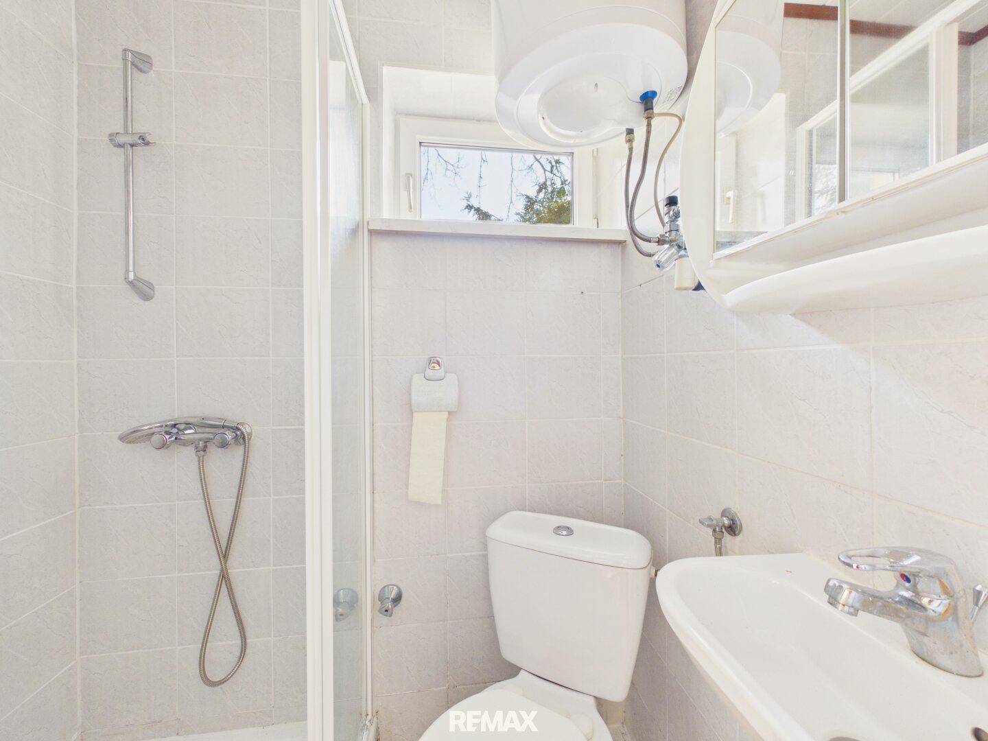 Kleines Badezimmer mit Dusche, Toilette, Waschbecken und Fenster.