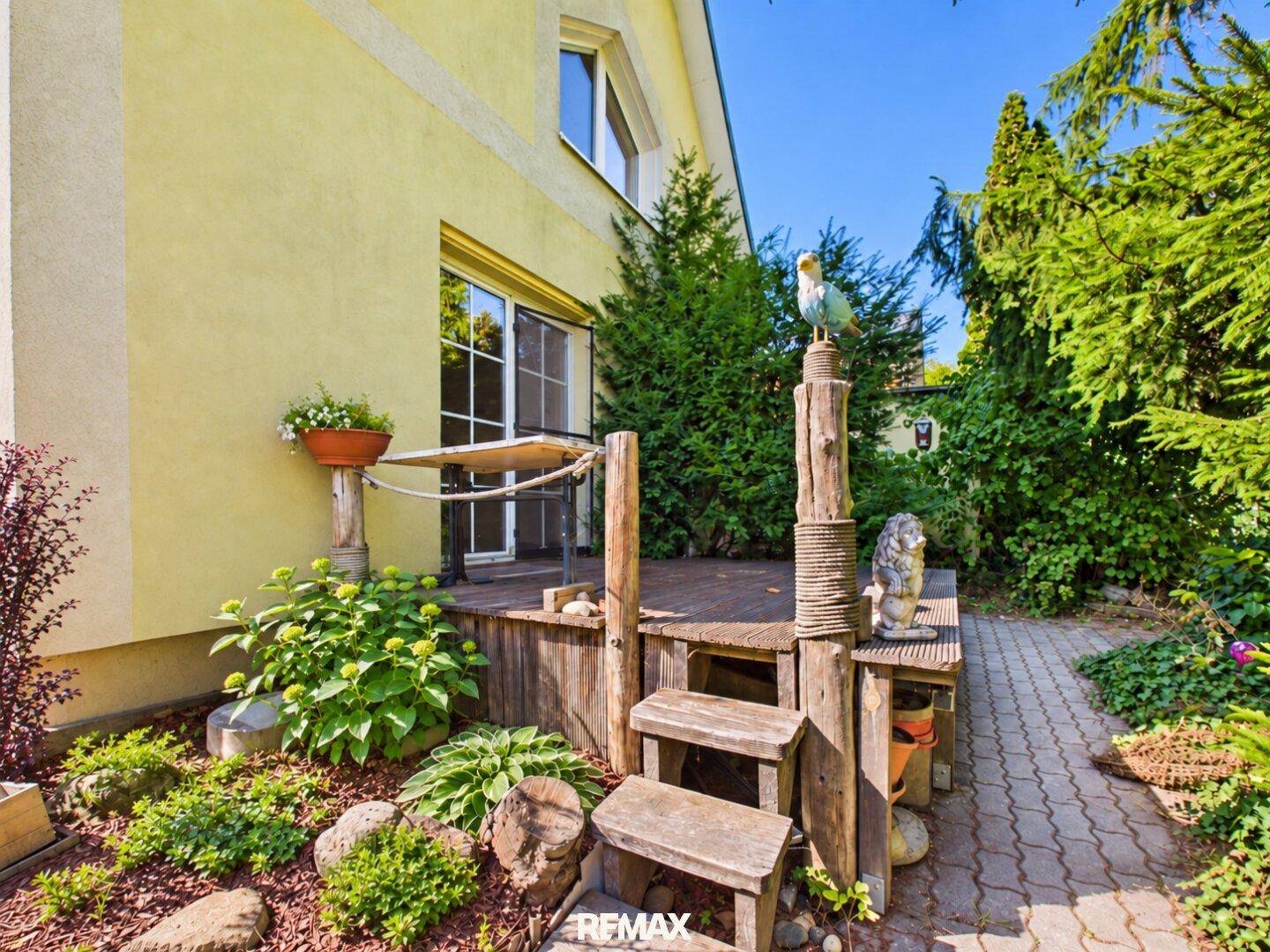 Holzterrasse mit Gartenbereich und dekorativen Elementen, umgeben von Grün.