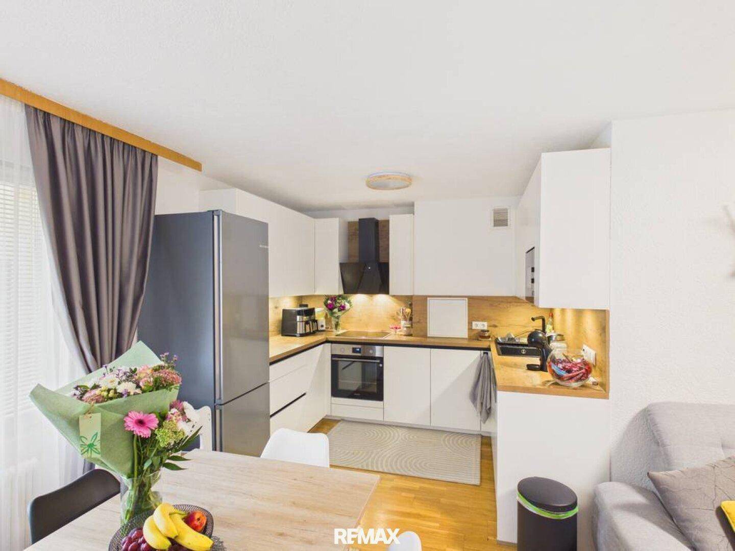 Moderne Einbauküche mit weißen Fronten, Holz-Arbeitsplatte und integrierten Geräten, offen zum Essbereich.