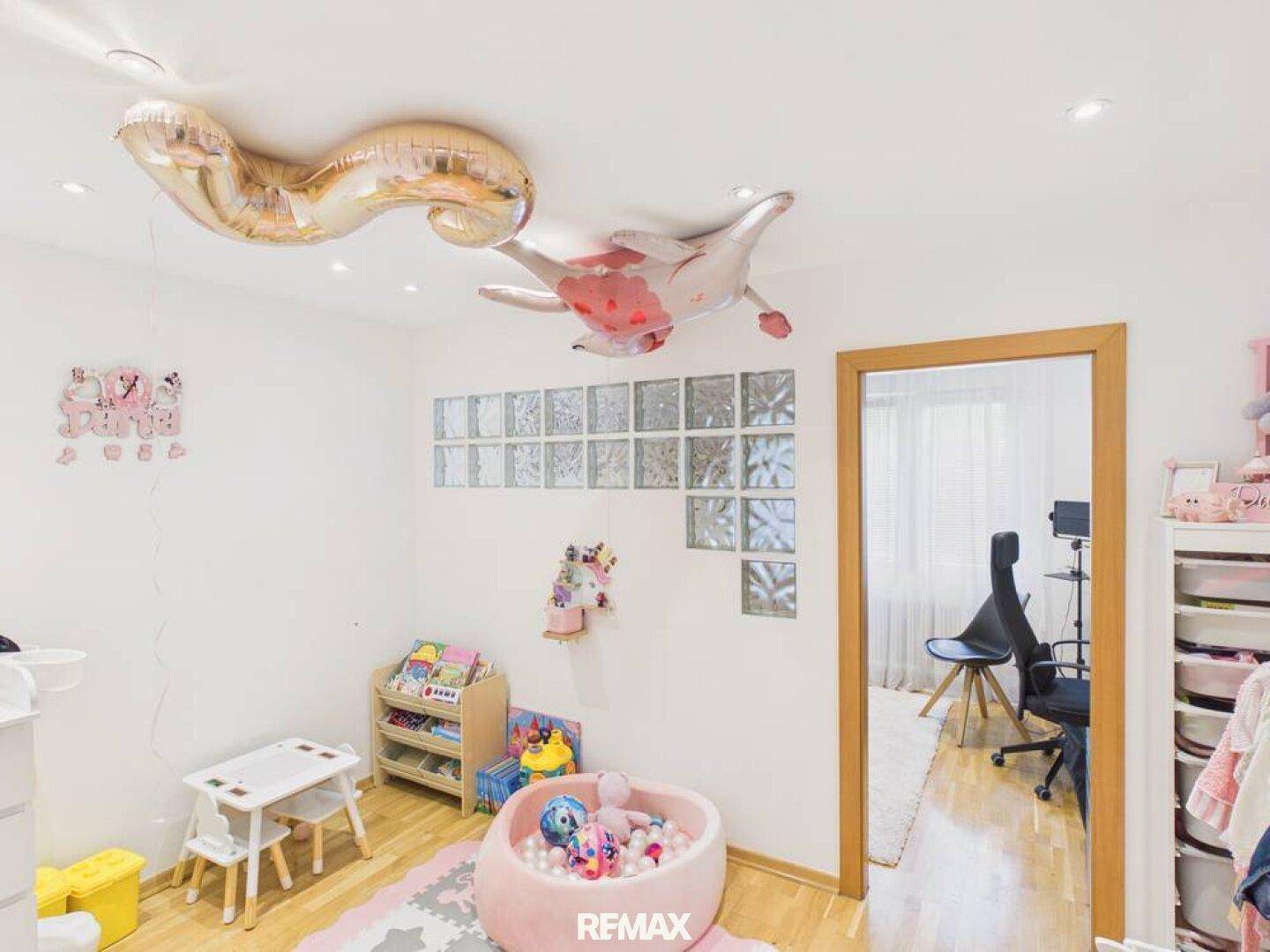 Freundliches Kinderzimmer mit Spielbereich, Holzboden und dekorativen Glasbausteinen an der Wand.