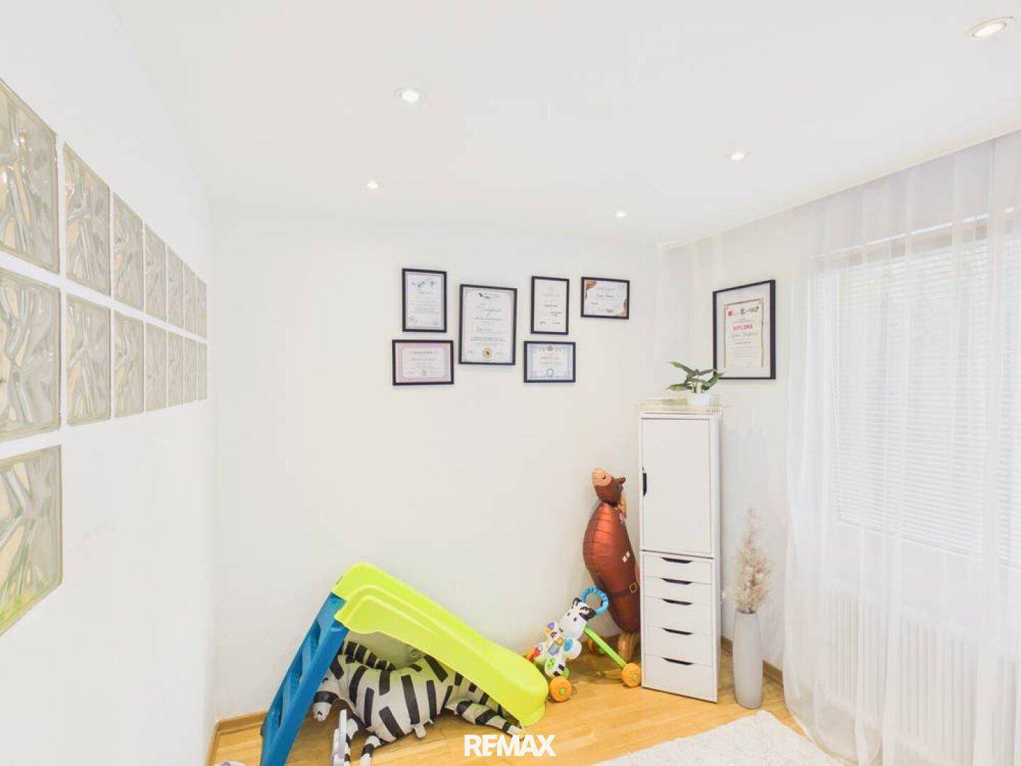 Helles Kinderzimmer mit Spielgeräten, Fenster und Holzboden, ideal zum Spielen und Lernen.
