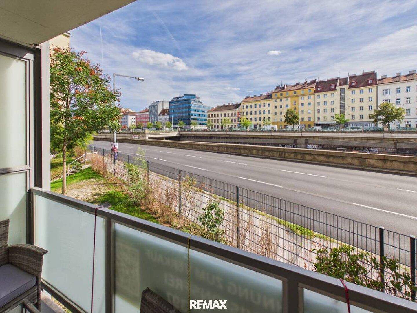 Balkon mit Blick auf eine belebte Stadtstraße und umliegende Gebäude, mit Sitzgelegenheiten.