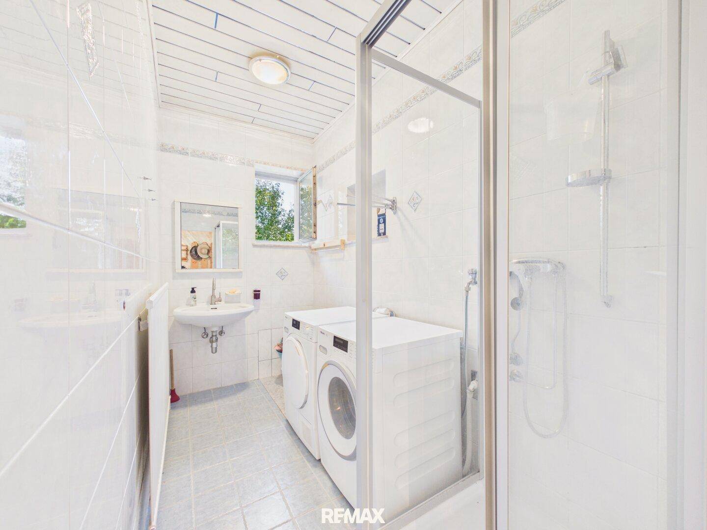 Funktionales Badezimmer mit Dusche, Waschmaschine und Fenster für Tageslicht.