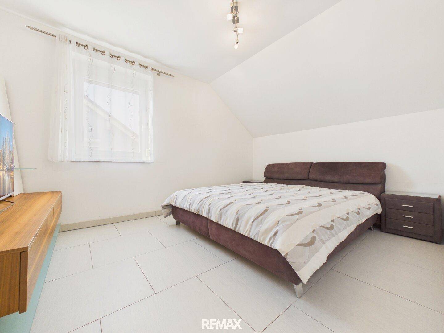 Helles Schlafzimmer im Dachgeschoss mit Doppelbett, Fliesenboden und schrägen Wänden für gemütliches Wohnen.