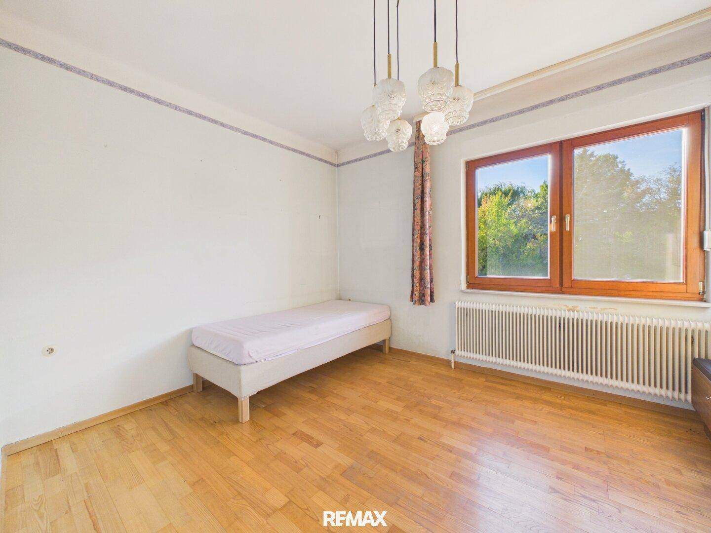 Schlafzimmer mit Einzelbett, Parkettboden und großem Fenster mit Blick ins Grüne.