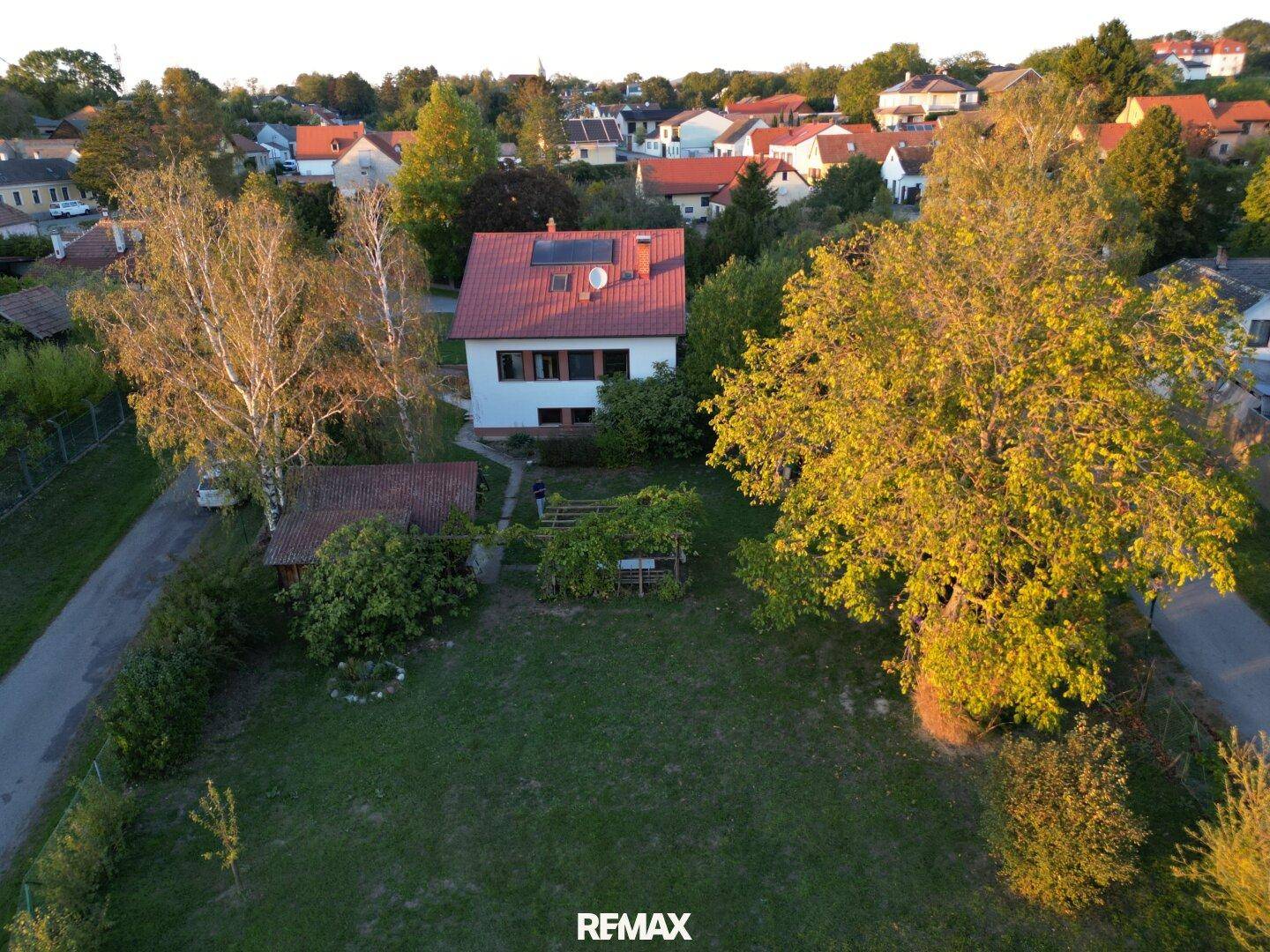 Drohnenansicht eines Hauses mit rotem Dach, Solaranlage und großem, gepflegten Garten.