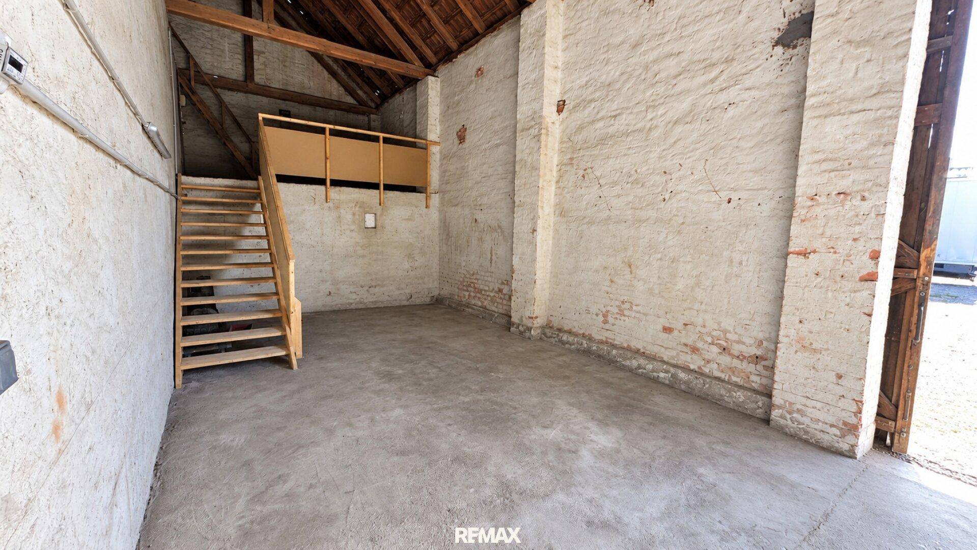 Leerer Garagenraum mit hohen Decken, einer Holztreppe und freiliegenden Holzbalken, ideal für Lagerung oder Werkstatt.