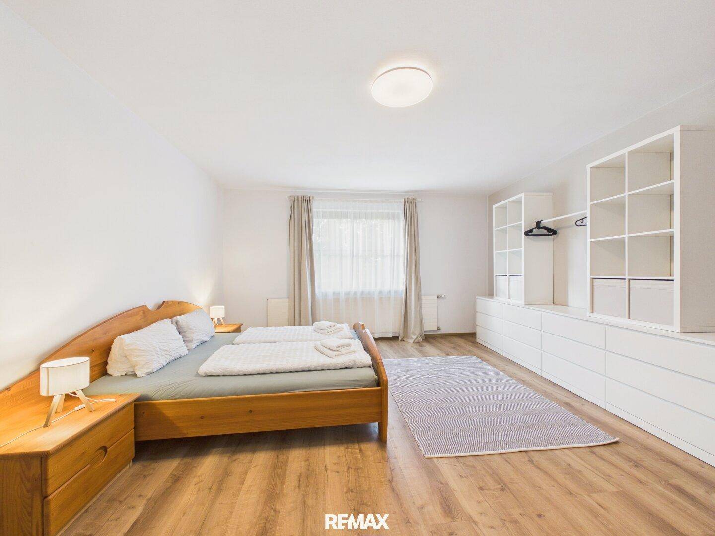 Geräumiges Schlafzimmer mit Holzbett, Kommoden und Fenster mit Vorhängen.