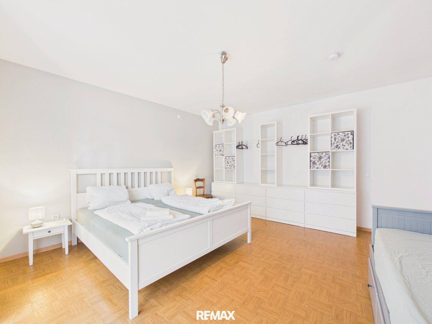 Helles Schlafzimmer mit weißem Doppelbett, Holzboden und offenen Regalsystemen.