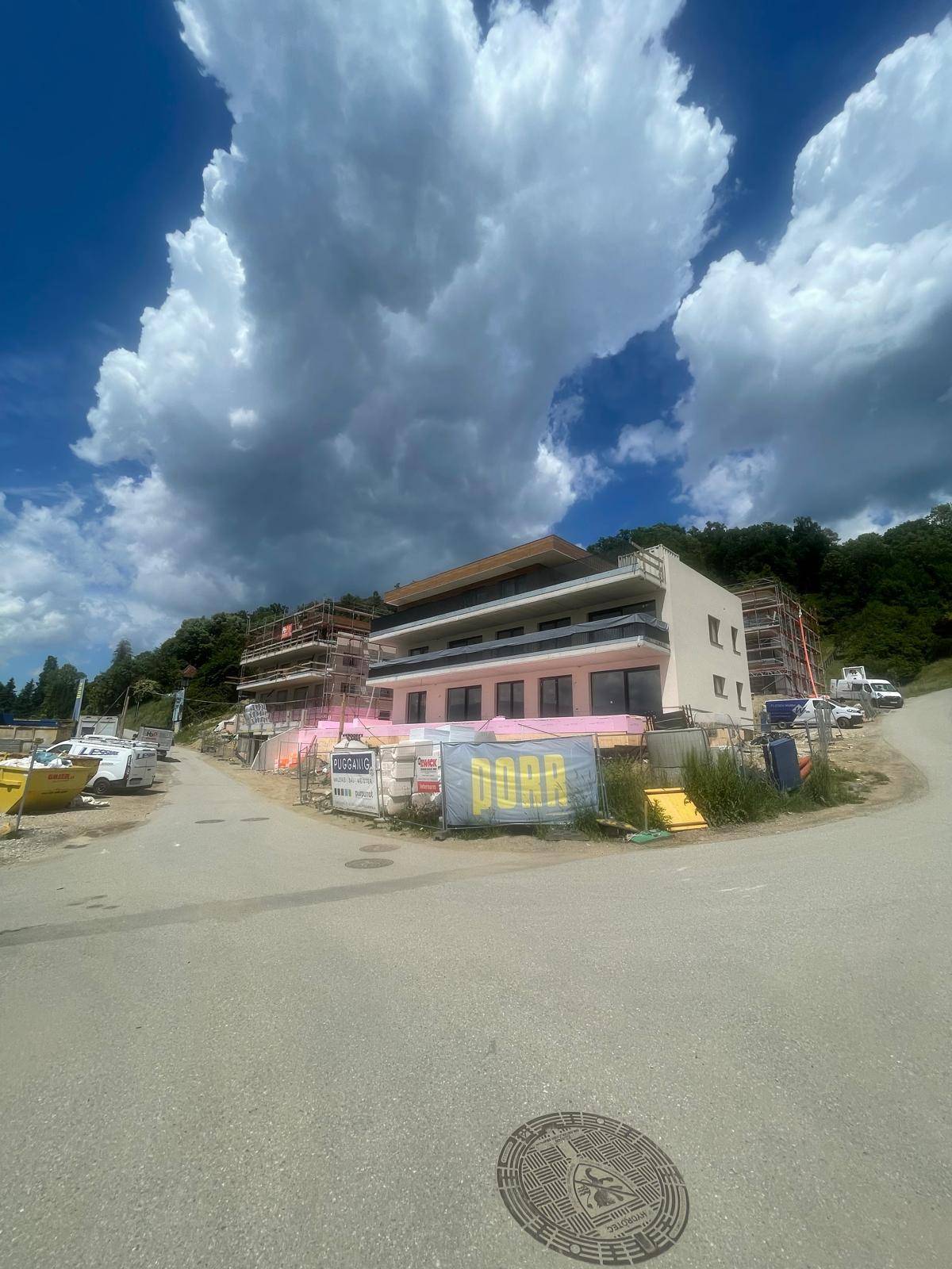 Baustelle eines neuen Wohngebäudes mit Gerüst und Baumaterialien unter blauem Himmel.