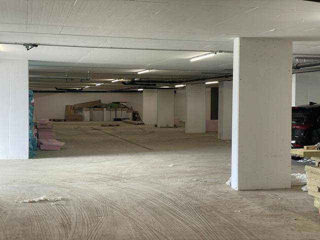 Geräumige Tiefgarage im Rohbau mit Betonstützen und Beleuchtung, bereit für den Ausbau.