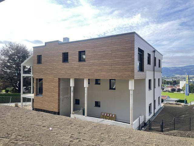 Neubau mit moderner Holz- und Putzfassade, umgeben von einer hügeligen Landschaft und Fernblick.