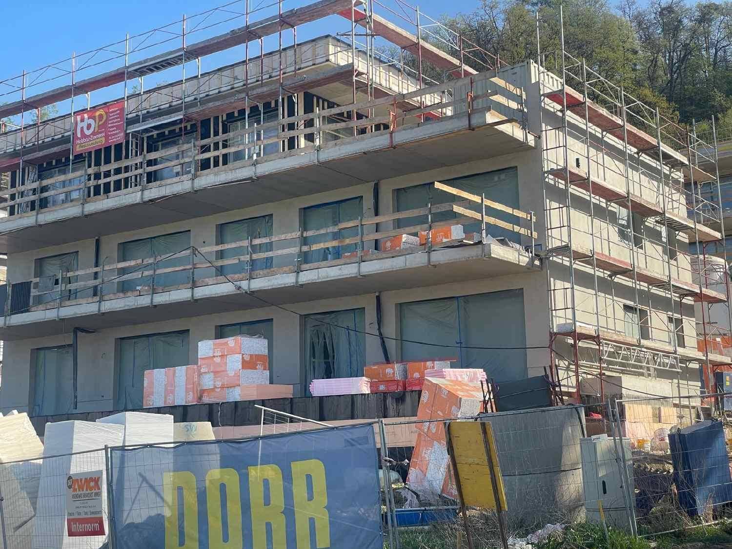 Neubau im Bauzustand mit Gerüst und Baumaterialien auf der Baustelle unter hellem Himmel.