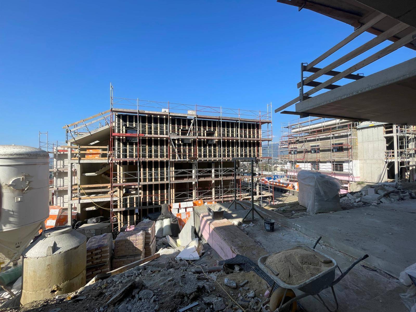 Baustelle mit mehreren im Bau befindlichen Gebäuden und Gerüsten unter blauem Himmel.