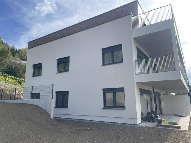 Seitenansicht des modernen Neubaus mit weißer Fassade, dunklen Fenstern und Eckbalkon.