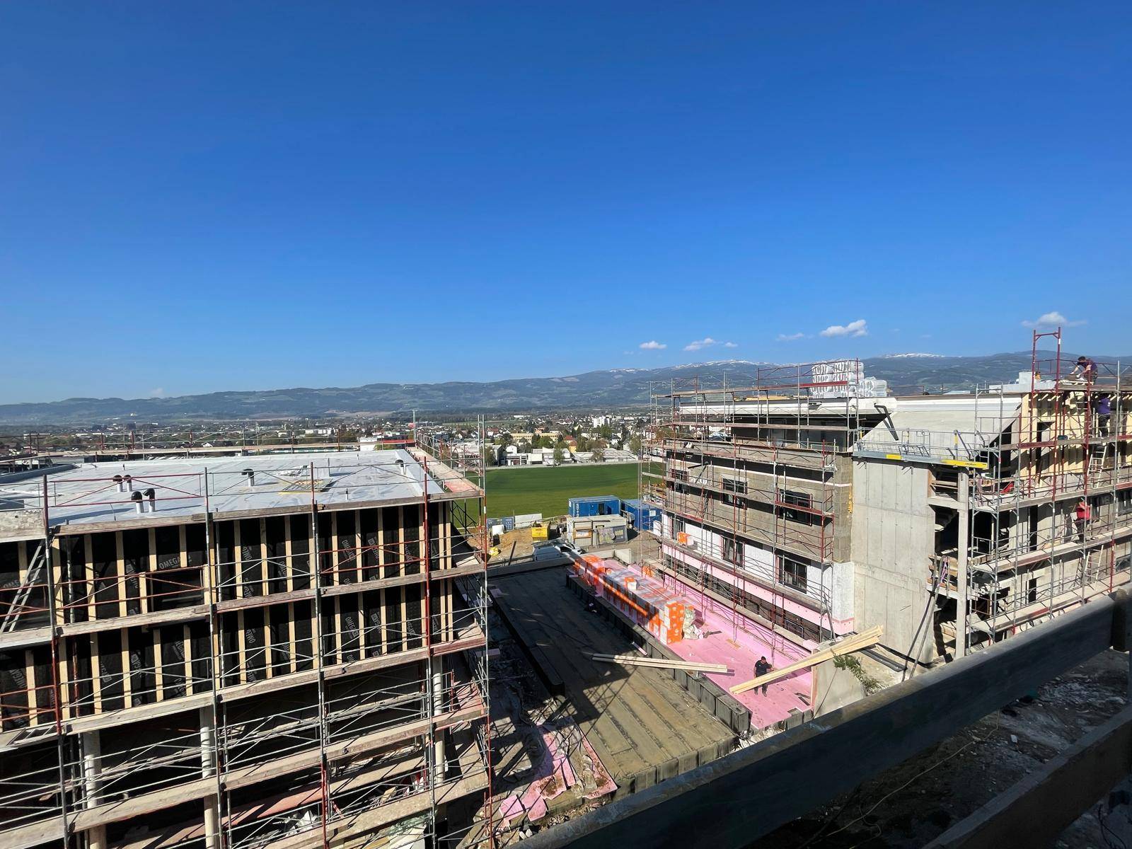 Baustelle mit mehreren Gebäuden im Bau und weitem Blick auf die Stadt und Berge.
