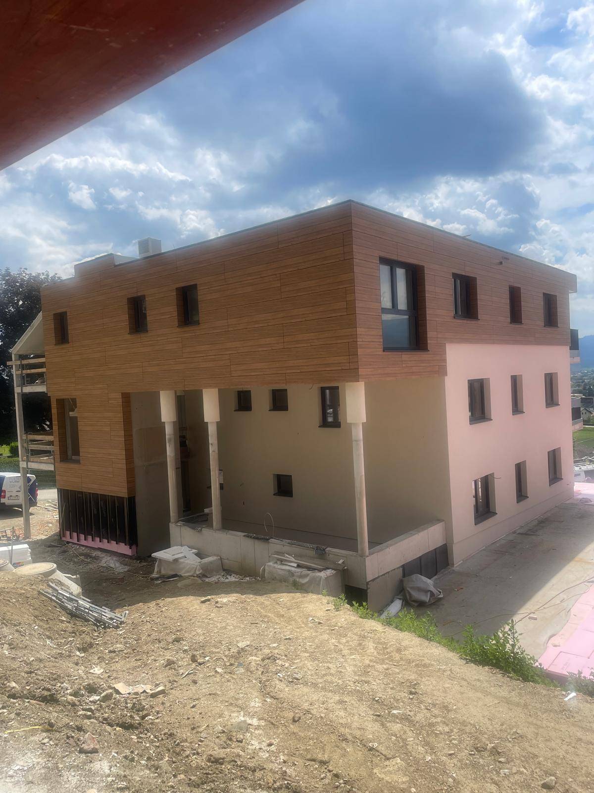Neubau in Bauphase mit Holzverkleidung und sichtbarer Dämmung unter bewölktem Himmel.