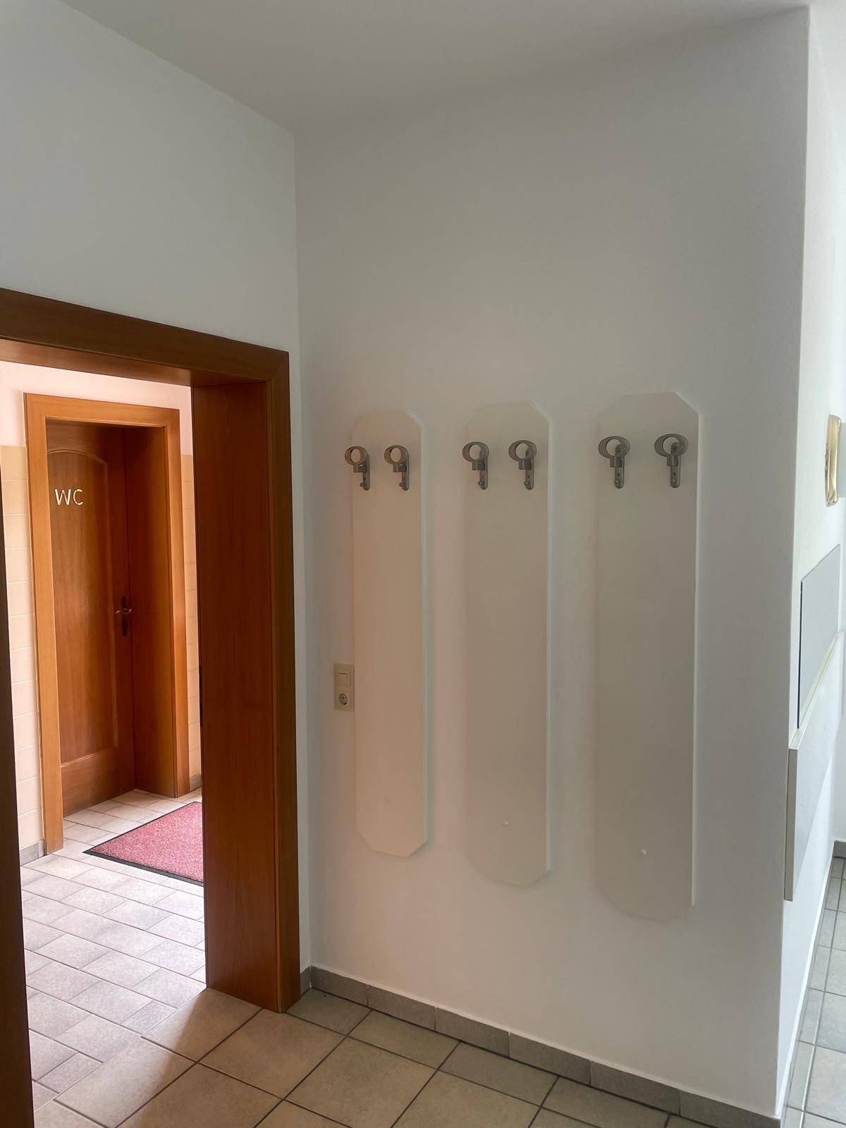 Flur mit Garderobenhaken an der Wand und Zugang zu einer Toilette.