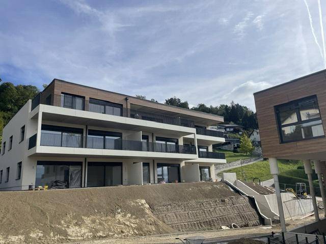 Gesamtansicht des modernen Apartmenthauses in Hanglage mit mehreren Balkonen und umliegender Natur.