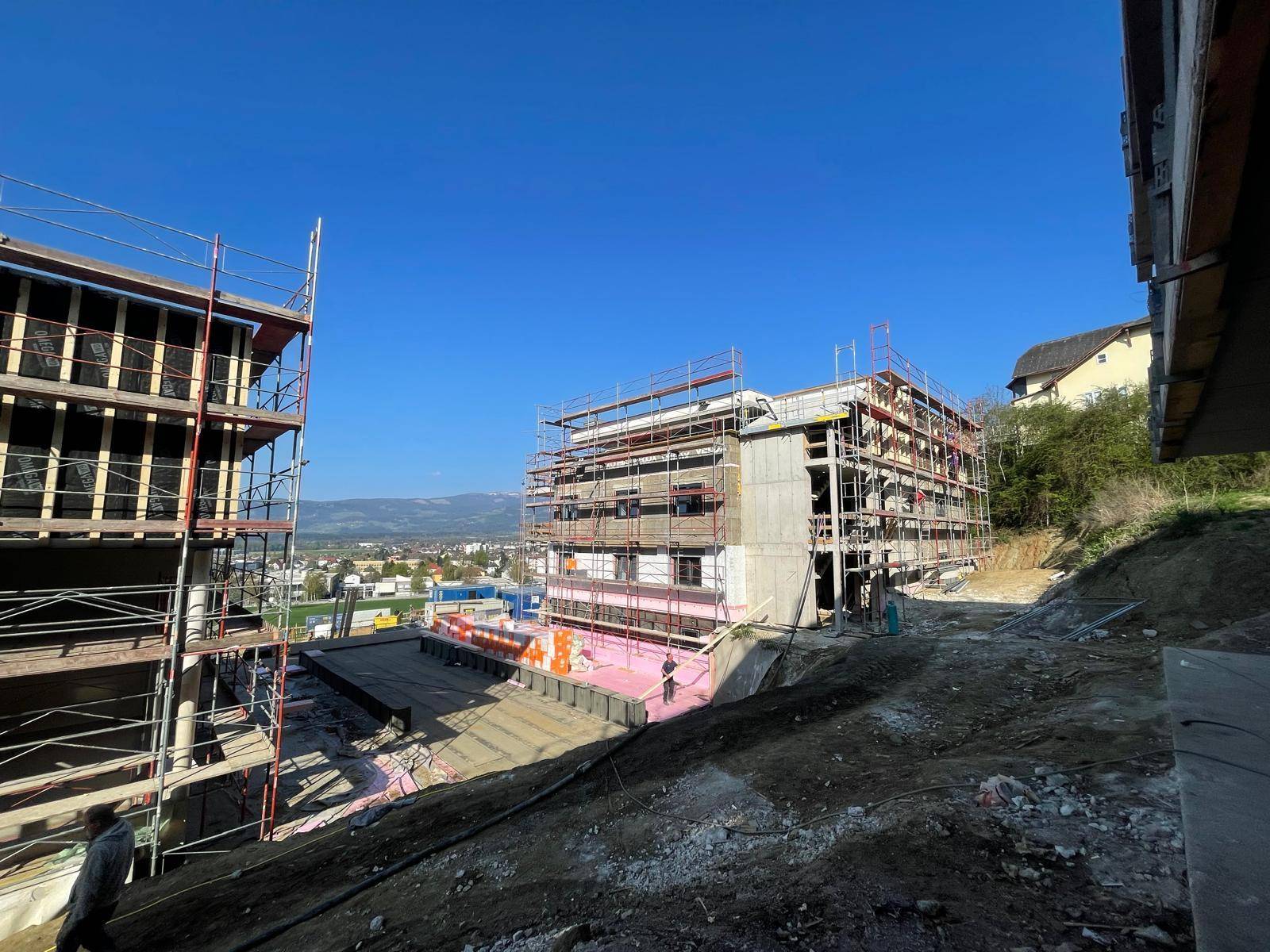 Weitläufige Baustelle mit mehreren im Bau befindlichen Gebäuden und Bergblick im Hintergrund.