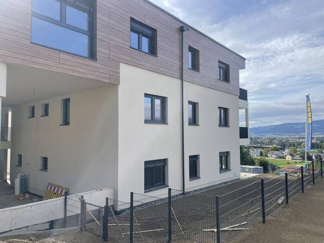 Ansicht des Neubaus mit gemischter Fassade aus Holz und Putz, mit Blick auf die umliegende Landschaft.
