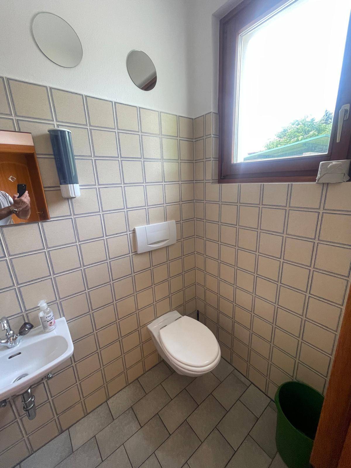 Kleines Badezimmer mit Toilette, Waschbecken, Fenster und beigefarbenen Fliesen.