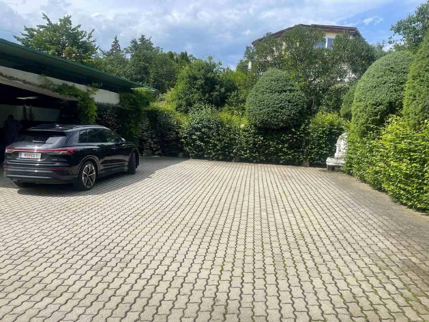 Gepflasterter Parkplatz mit einem Auto, umgeben von Hecken und Bäumen.