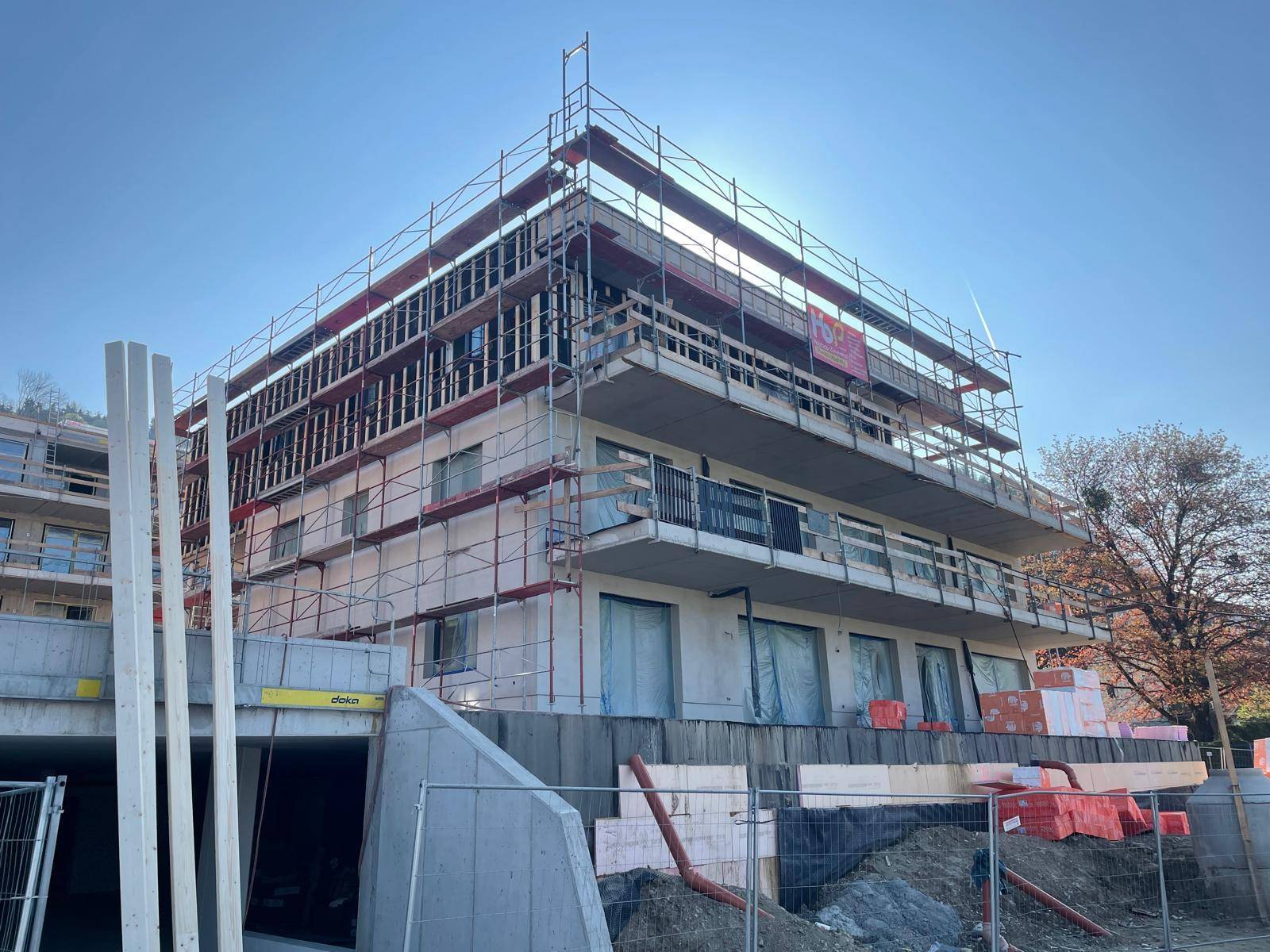 Rohbau eines modernen Gebäudes mit Gerüst und sichtbaren Bauelementen bei Sonnenschein.