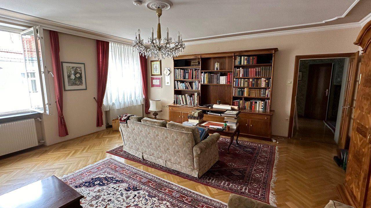 Gemütliches Wohnzimmer mit Parkettboden, großem Bücherregal und Kronleuchter.