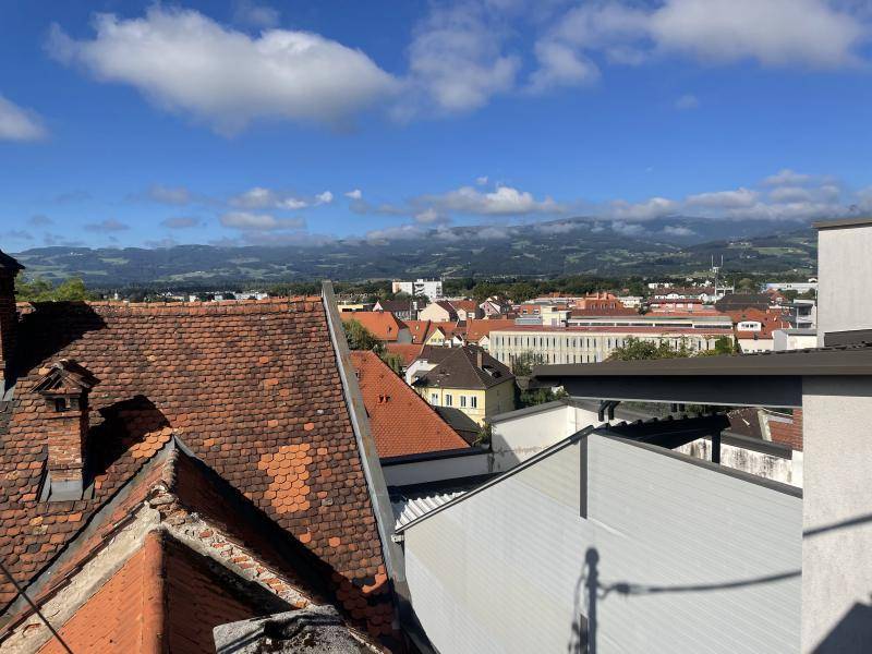 Panoramablick über die Dächer der Stadt mit Bergen im Hintergrund unter blauem Himmel.