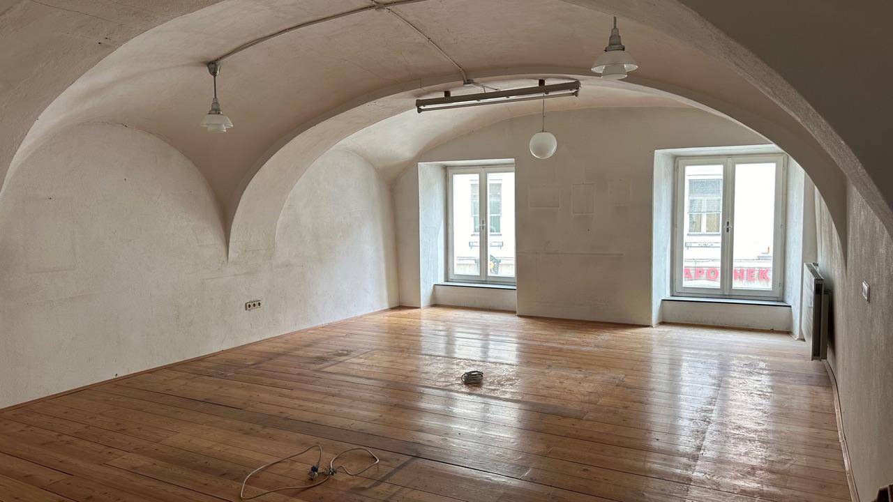 Geräumiger Raum mit Gewölbedecke und Holzdielenboden, hell durch zwei Fenster.