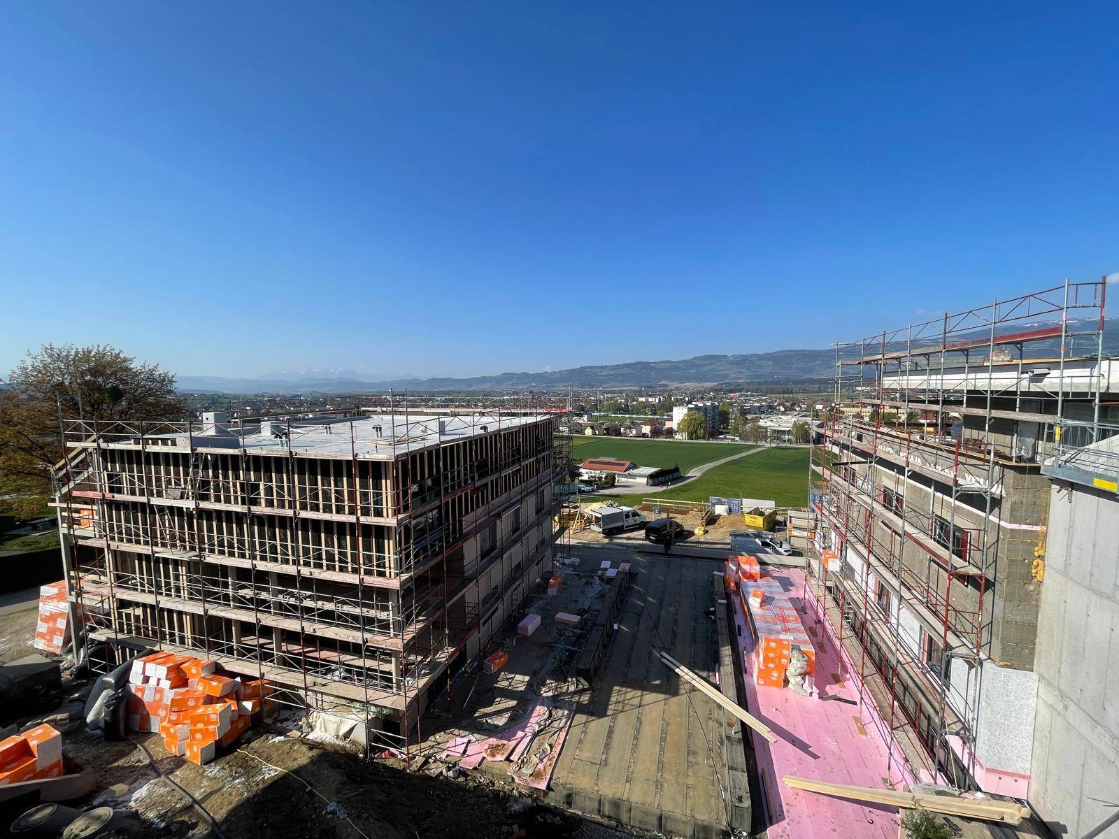 Baustelle eines neuen Wohngebäudes mit Gerüsten und Baumaterialien unter blauem Himmel.