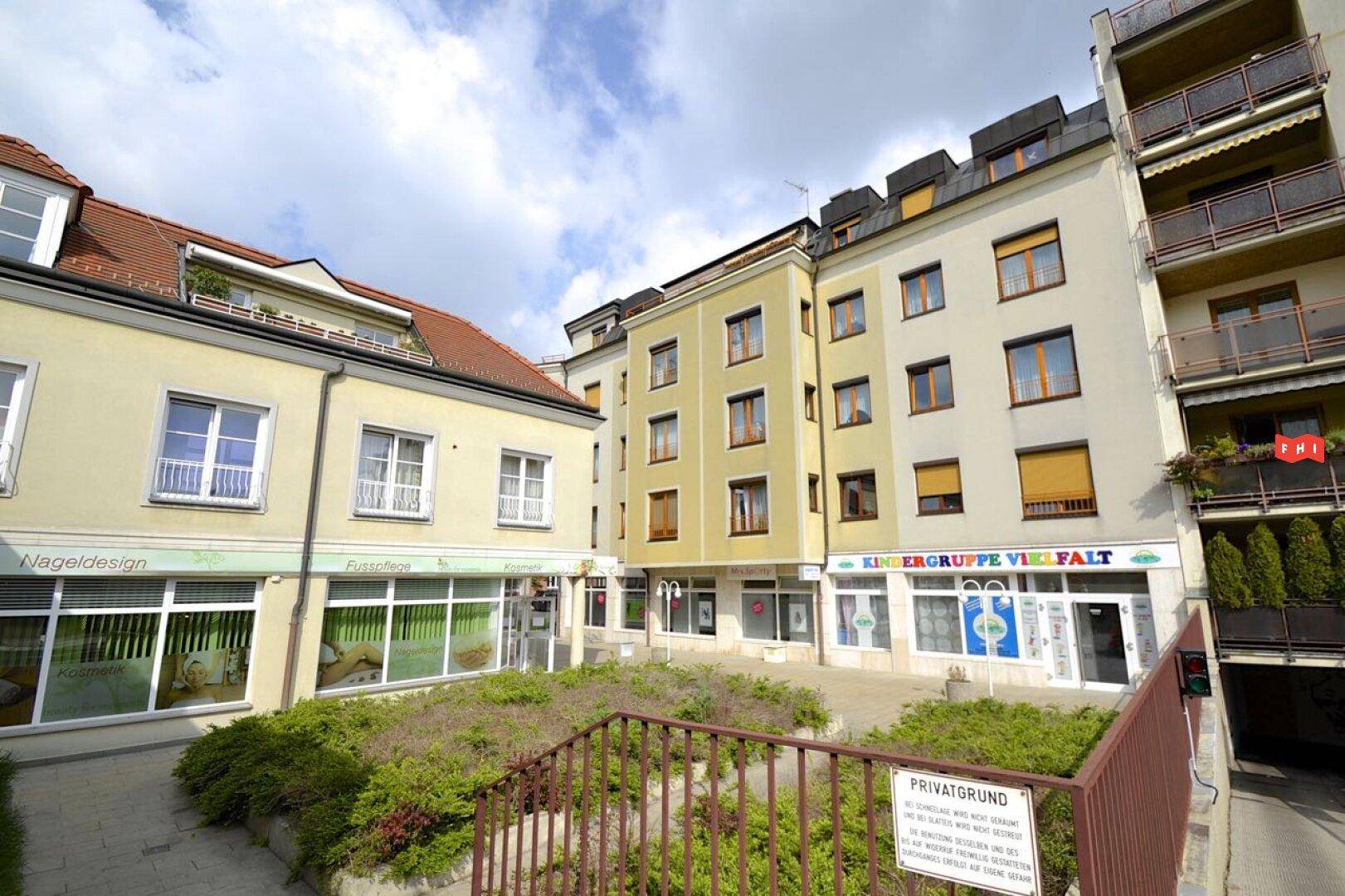 Außenansicht eines Wohngebäudes mit Geschäften im Erdgeschoss und einem Innenhof.