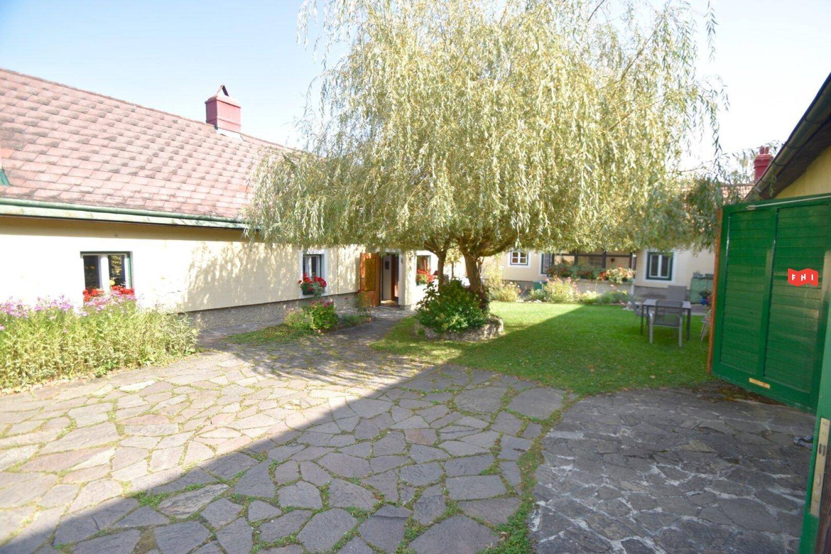 Idyllischer Innenhof mit Natursteinpflaster, einem großen Baum und Sitzgelegenheiten.