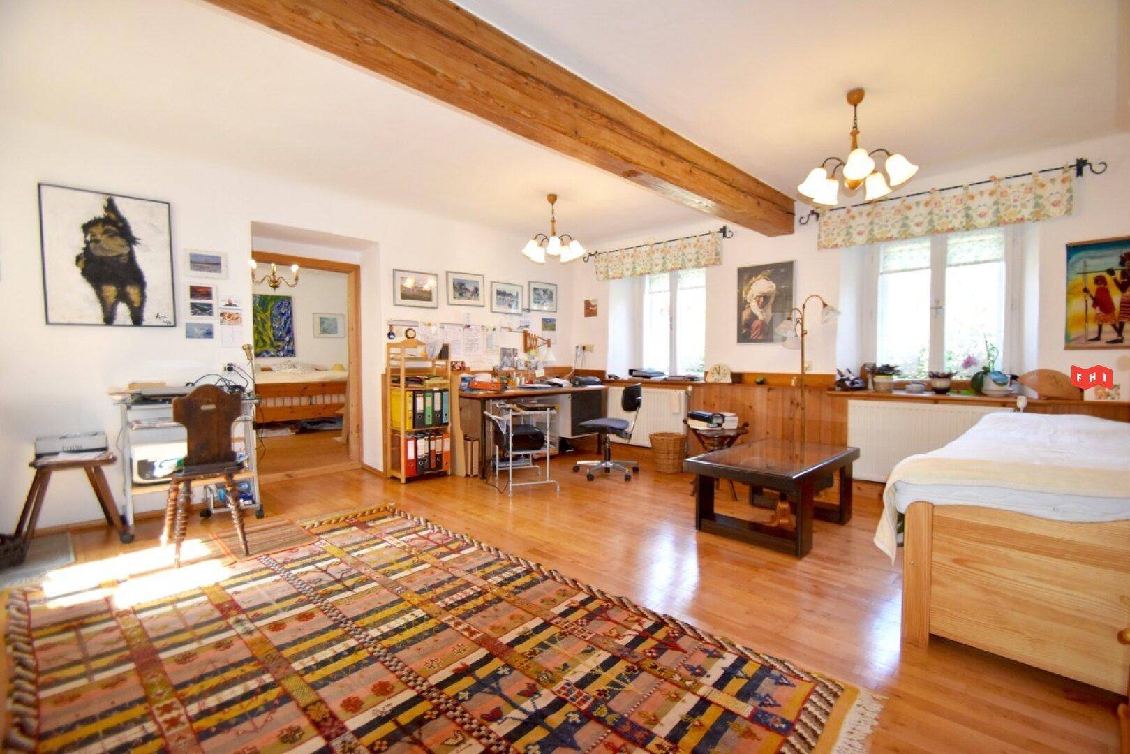 Großes Schlafzimmer mit Holzboden, sichtbaren Deckenbalken und integriertem Arbeitsbereich.