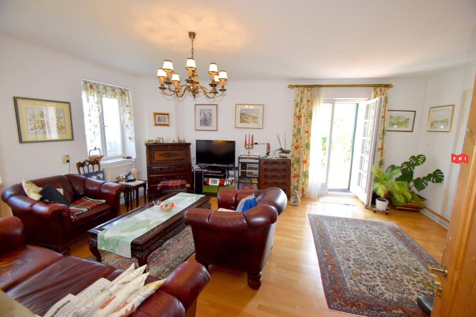Geräumiges Wohnzimmer mit Ledersofas, Holzboden und Zugang zum Garten.