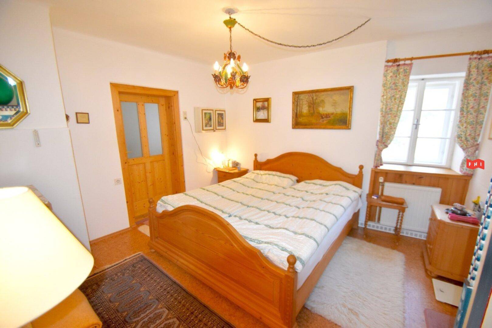 Gemütliches Schlafzimmer mit Holzbett, Parkettboden und Fenster mit Vorhängen.