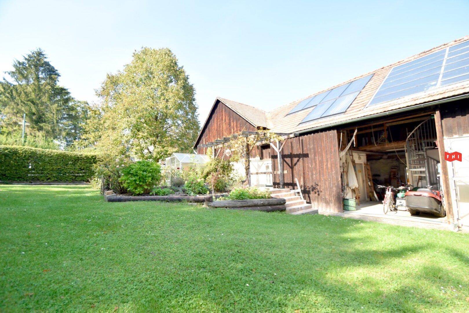 Großer Gartenbereich neben dem Gebäude mit offenem Scheunentor und Photovoltaikanlage.