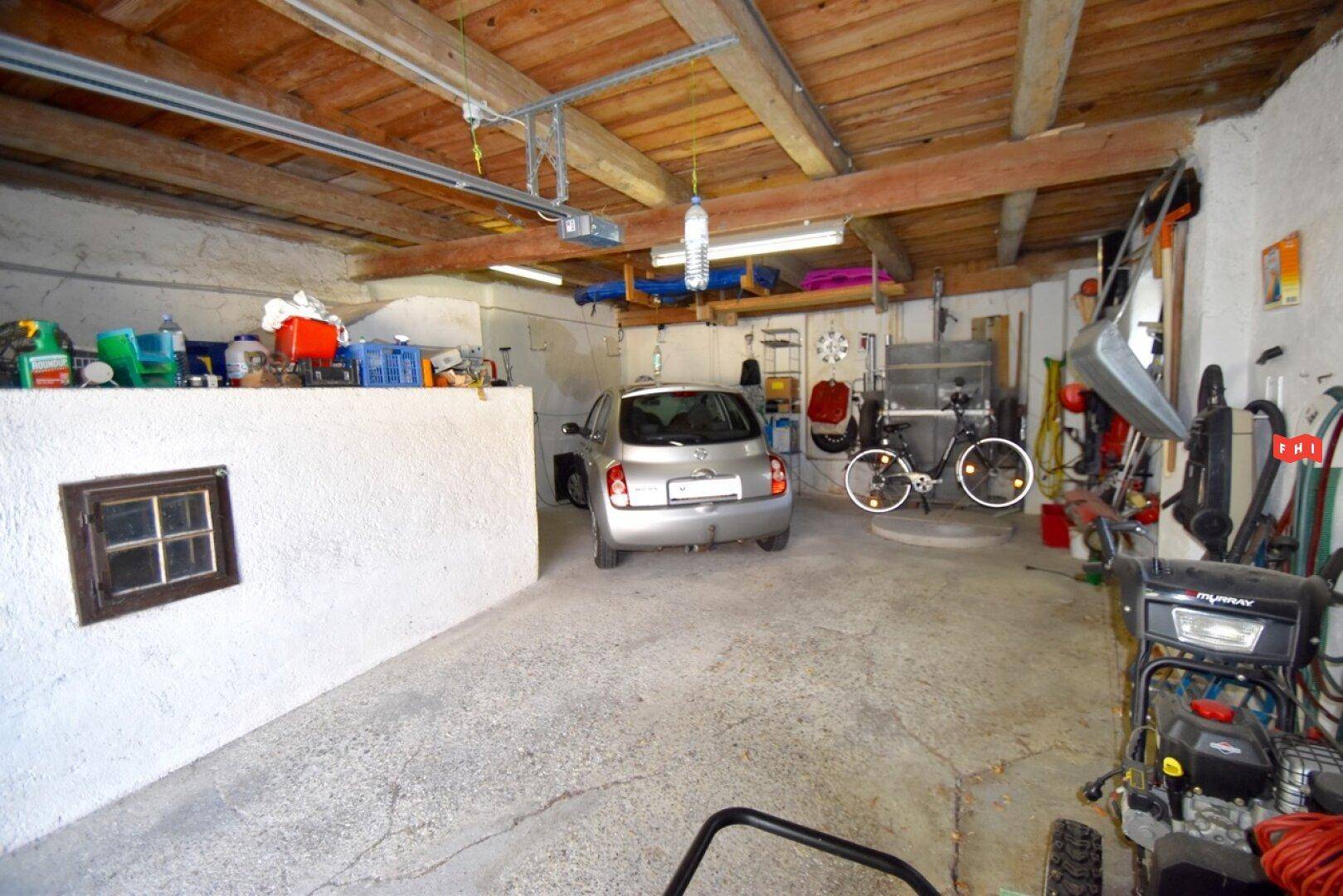 Geräumige Garage mit Betonboden und Platz für ein Fahrzeug und Fahrräder.